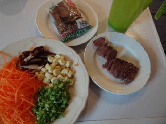 Légumes, viande émincée, sachet d'épices pour pho et les nouilles qui trempent dans un pichet